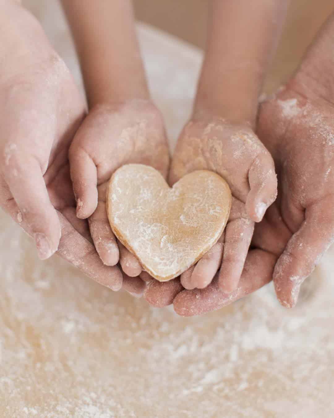 Adult and child hands holding a heart‑shaped piece of dough on a floured surface