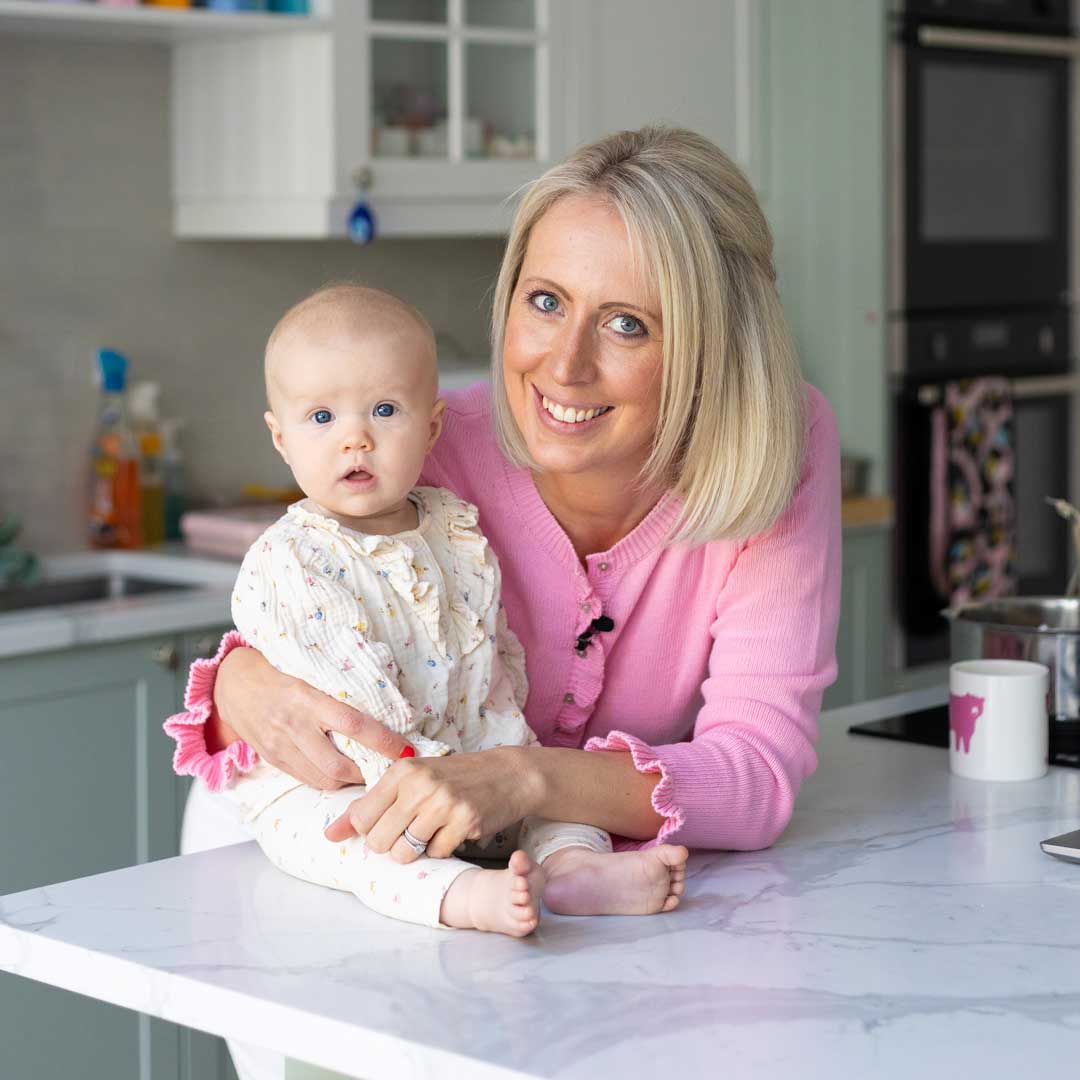 Mother holding her unsettled baby in a kitchen, looking tired and seeking support with infant sleep.