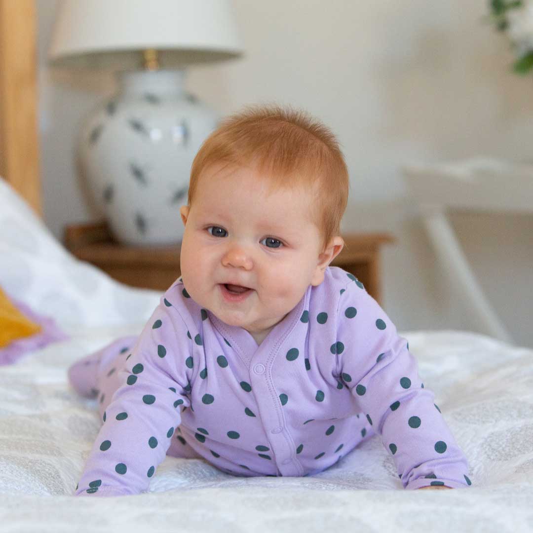 Baby lying on a bed during tummy time, looking up with alertness in a calm bedroom setting.