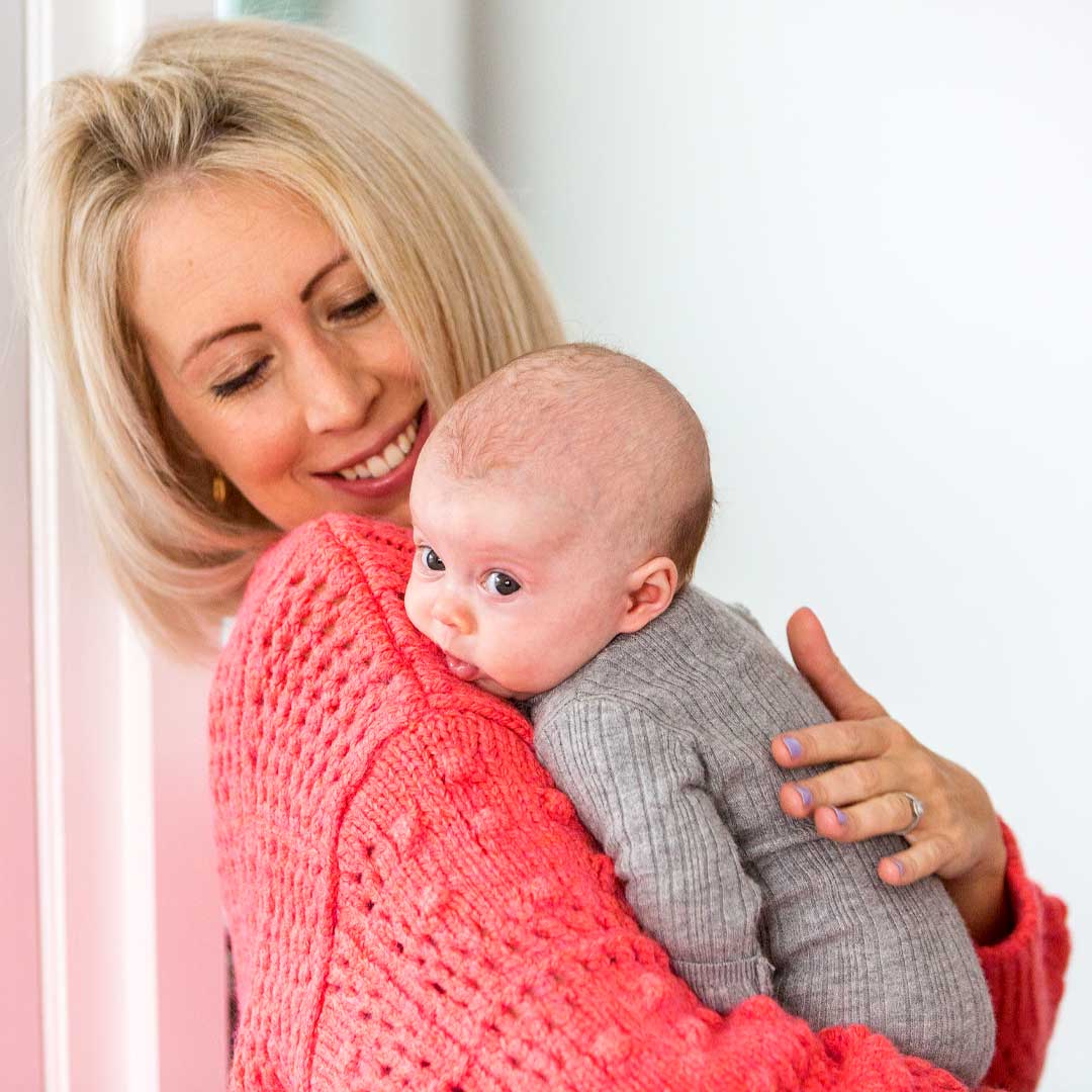 Adult holding a baby against their shoulder in a calm indoor setting, offering comfort and support.